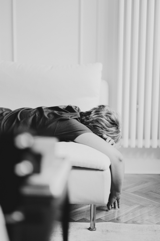 Schwarz-weiße Aufnahme: Person liegt erschöpft auf dem Sofa. Nur Hinterkopf und herabhängender Arm zu sehen