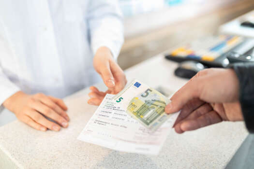 Eine Apotheker nimmt die Zuzahlung eines Patienten an der Kasse an