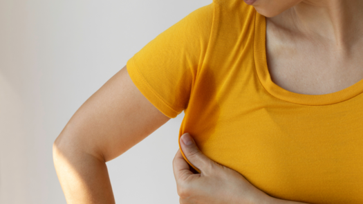 Frau hält das gelbe T-Shirt von ihrer Achsel weg - die Stelle hat einen Schweißfleck